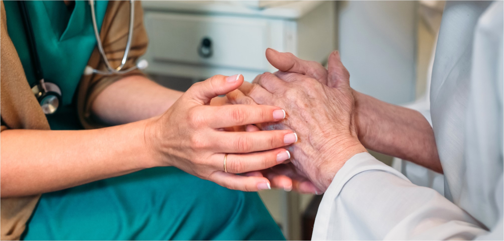 two people hold hands. one set of hands appear to be nurse's hands, and the other appear to be the patient's hands
