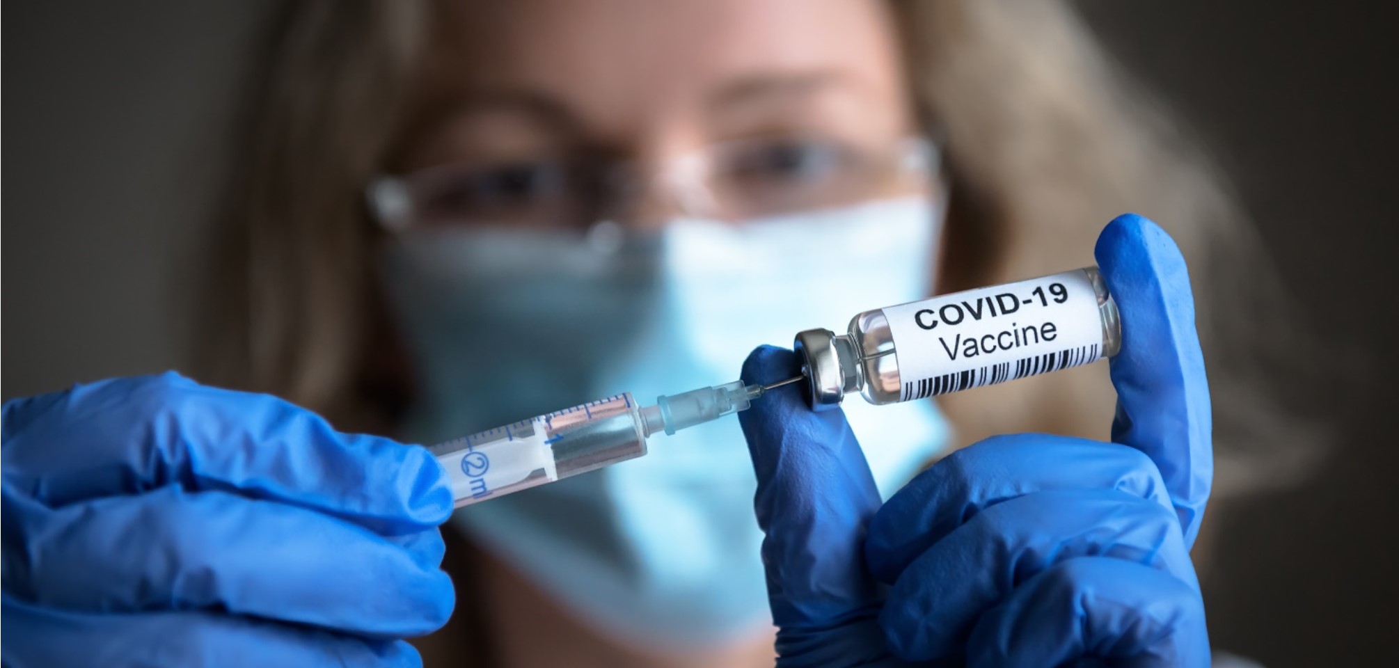 close up of a woman wearing surgical gloves and holding a vial of COVID19 vaccine