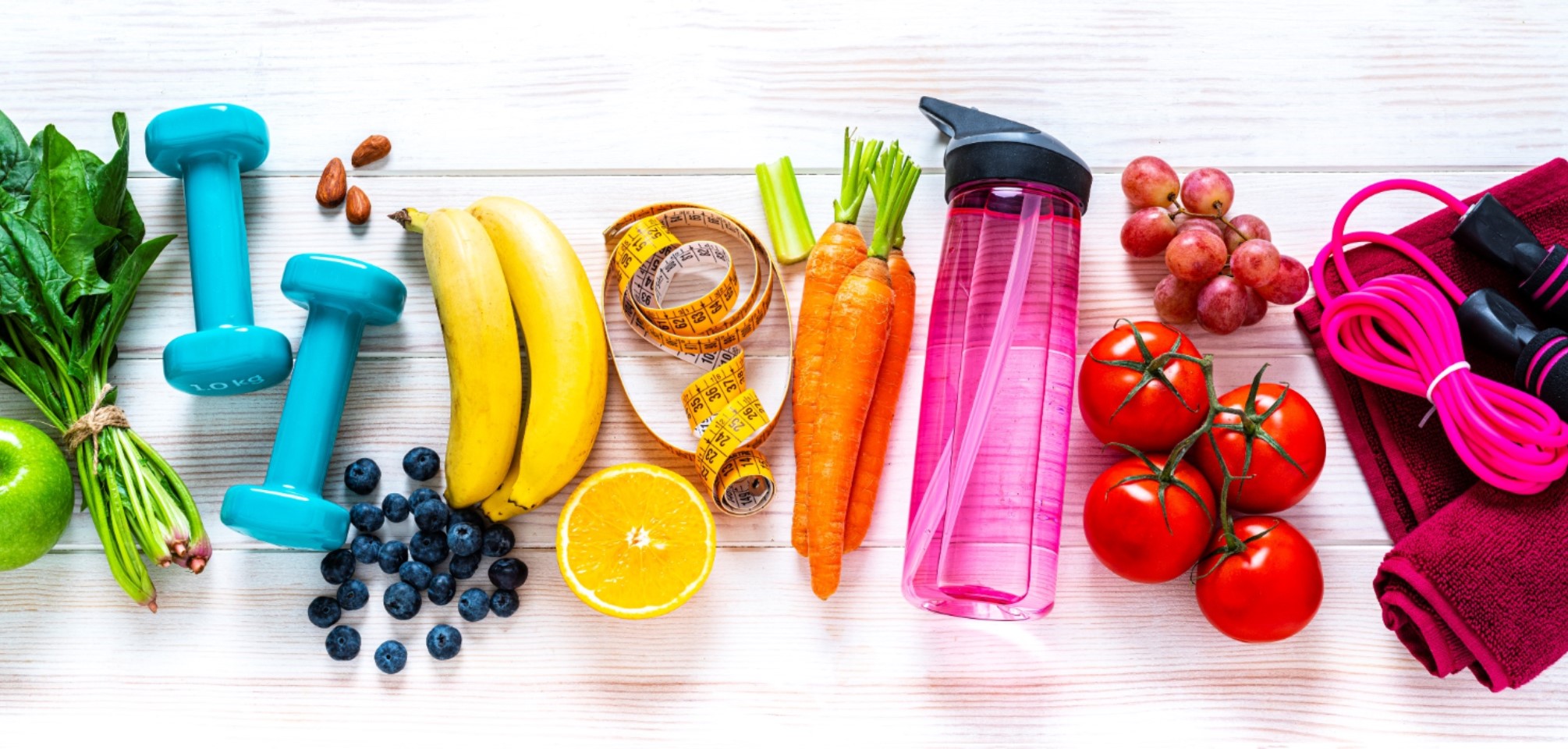 photo features a mix of fruits and vegetables alongside hand weights, a water bottle and other fitness items